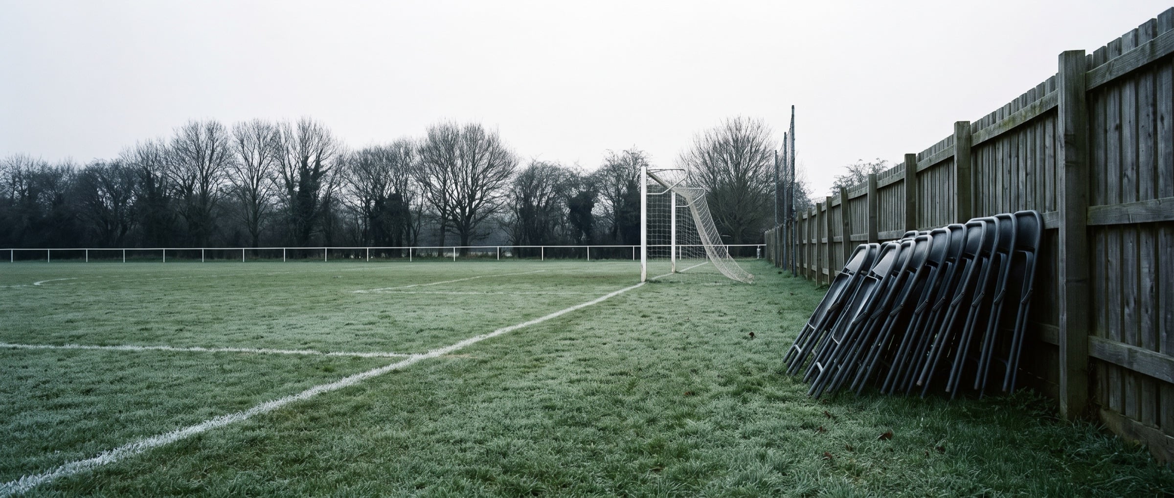 An empty grass pitch on a cool morning, lines freshly marked, before anyone arrives.